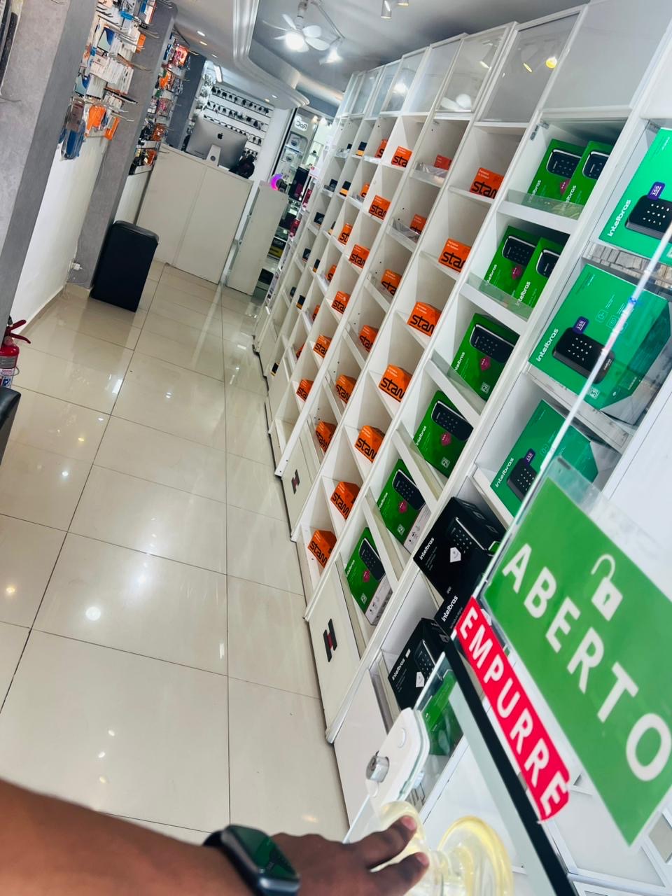 Interior da loja Locksmithcell com prateleiras de fechaduras digitais Intelbras e placa Aberto